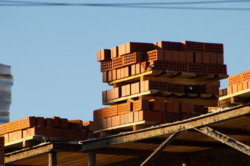 Stack of Red Bricks on an Unfinished Construction Site Against a Clear Blue Sky