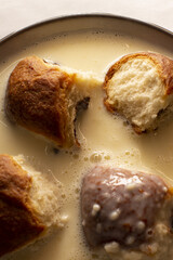 Brioche bites soaking in warm custard closeup showing torn golden rolls and creamy milk pooling around soft airy crumb, subtle