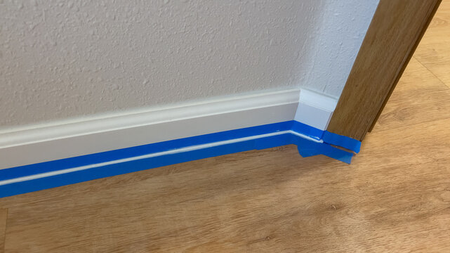 Painter's tape along white baseboard corner