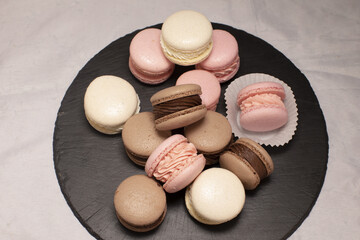 pastel macarons on black slate plate, neat pile of pink, brown and ivory cookies creating soft gourmet mood with delicate almond