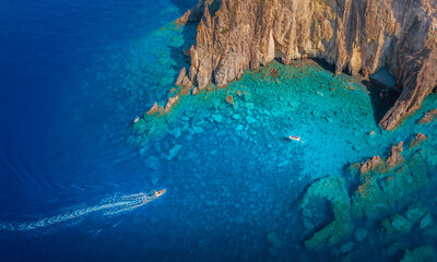 Aerial view of the turquoise waters gently lapping against the rugged, sun-kissed cliffs, boats cutting through the deep blue sea, Panarea, Sicily, Italy.