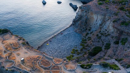 Aerial view of a rugged coastline meeting the tranquil turquoise sea, contrasting with the ancient ruins scattered along the cliffs, Panarea, Sicily, Italy.