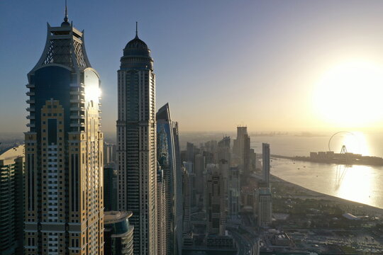 Panoramic aerial view of Dubai Marina skyscrapers and Jumeirah Beach Residence at sunset, featuring the Ain Dubai Ferris wheel and the Arabian Gulf coastline.