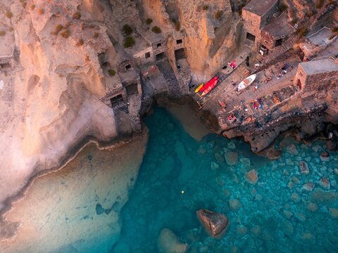 Aerial view of the rugged coastline, where ancient stone structures meet the turquoise sea, creating a striking contrast against the warm-toned cliffs, Salina, Sicilia, Italy.