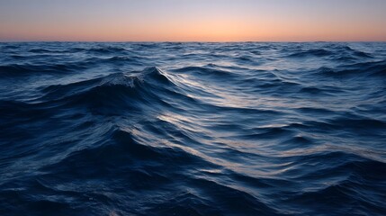 A vast ocean surface with gentle waves under a twilight sky at sunset or sunrise reflecting the soft orange glow on the horizon