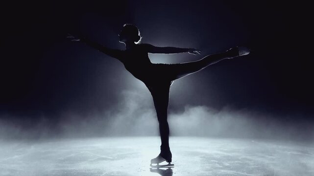 Silhouette of a figure skater performing an elegant spiral on the ice. Female athlete gliding in an arabesque pose with dramatic backlighting and fog. Winter sport and artistic performance concept