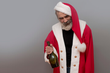 Bad Santa Claus drunkard with bottle of wine on gray background. Natural beard, red hat, suit.