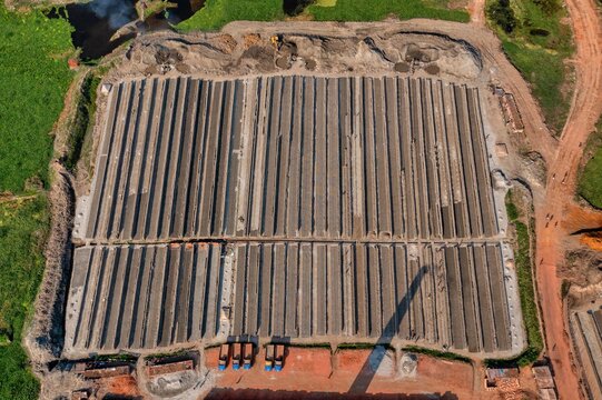 Aerial view of rows of drying bricks casting long shadows under the sun, a stark contrast to the green fields surrounding the brickyard, Aminbazar, Dhaka Division, Bangladesh.