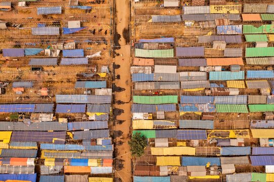 Aerial view of tightly packed, colorful shelters creating a vibrant mosaic across the landscape, divided by a stark, barren pathway, Aminbazar, Dhaka Division, Bangladesh.