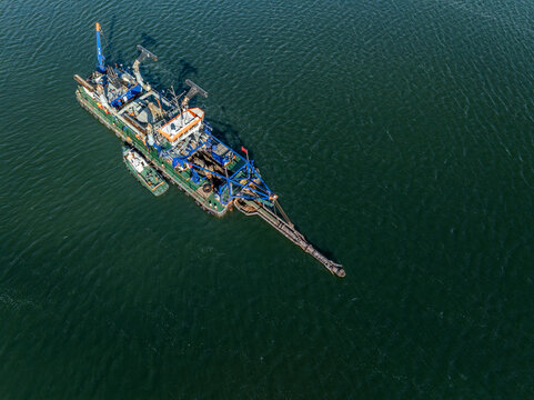 Aerial view of a dredging vessel floating on the calm waters, casting a long shadow on the rippled surface, Haven van IJmuiden, Velsen-Noord, Netherlands.