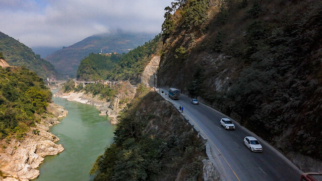Aerial view of the Prithvi Highway snaking along the Trishuli River, with vehicles moving alongside steep, verdant hills, Pokhara, Nepal.