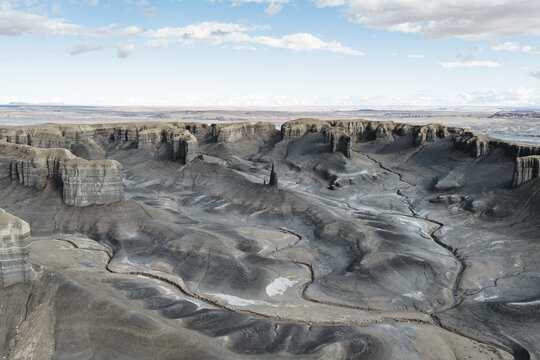 Aerial view of a rugged, desolate landscape where the stark contrast between the dark, furrowed earth and the pale, striated mesas creates an otherworldly scene, Hanksville, Utah, United States.