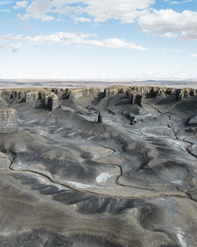 Aerial view of a stark, otherworldly landscape sculpted by time and erosion, revealing winding paths etched into the earth under a vast sky, Hanksville, Utah, United States.