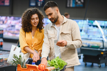 Couple checking grocery receipt while shopping in supermarket