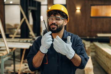 Talking by walkie talkie. Portrait of a male carpenter posing in a woodworking workshop