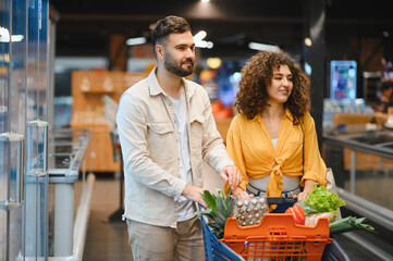 Young couple shopping groceries in modern supermarket aisle