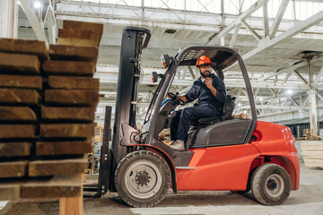 Heavy material, lifting the planks. Warehouse worker operating a forklift while handling wooden materials