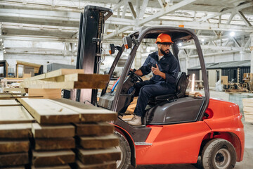 Transportation of the planks. Warehouse worker operating a forklift while handling wooden materials