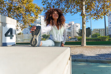 Young black woman stretching leg in urban park, preparing for fitness workout and outdoor exercise