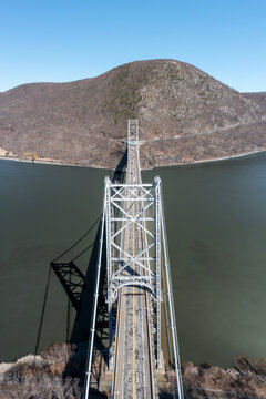Aerial view of the Bear Mountain Bridge stretching across the Hudson River, framed by the stark, leafless trees against a clear blue sky, Bear Mountain, New York, United States.