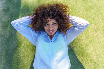 Young smiling woman performing crunches on green sports field, enjoying outdoor fitness workout