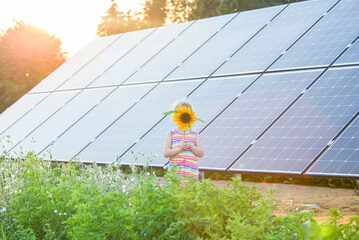 
Young 6 year old blonde girl child standing in front of small solar panel farm in countryside. Renewable energy concept. Sun lens flare.
