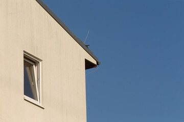 A corner of a distinctive building featuring a prominent window, complemented by a beautiful blue sky that stretches in the background