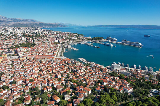 Aerial view of terracotta rooftops cascading towards the shimmering Adriatic, where cruise ships nestle in the harbor against a backdrop of distant mountains, Split, Split-Dalmatia County, Croatia.