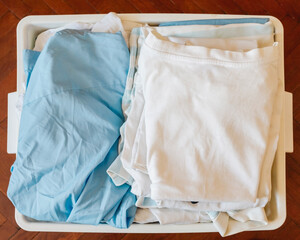 Freshly Folded White And Blue Laundry In Plastic Basket On Wooden Floor. Concept For Household Chores, Daily Routine, Clean Textile Care, And Efficient Home Laundry Organization