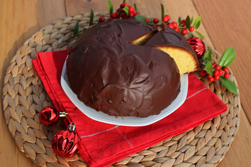Italian traditional sweet cake called Parrozzo made with almonds and semolina on a plate on wooden table with Holly branches with red berries and red Christmas glass balls with copy space
