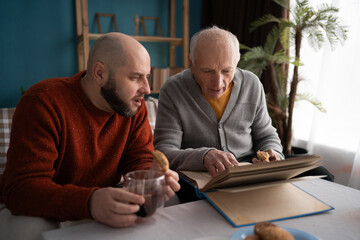 loving adult son with his elderly senior father looking family photograph photos at home. fathers day.