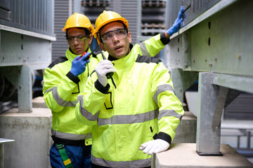 Engineers talk on a walkie talkie and inspecting machinery, wearing hard hats and safety gear in the factory