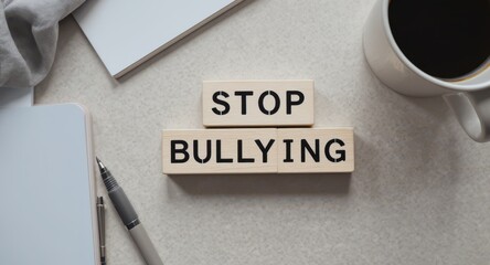 Wooden blocks spelling STOP BULLYING on office desk with notebook, pen, and coffee cup, concept of workplace awareness, respect and inclusion against harassment and discrimination