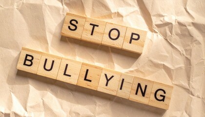 Wooden blocks spelling STOP BULLYING arranged diagonally on crumpled beige paper background with warm lighting, concept of anti-bullying awareness, respect and social empathy