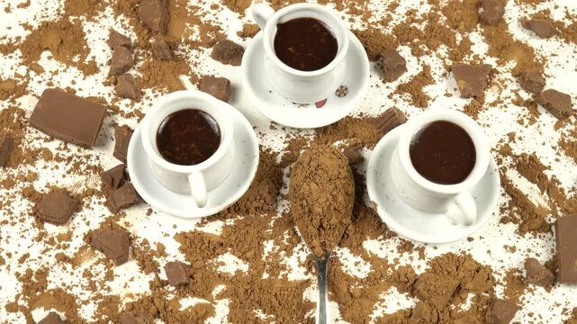 White cups with hot chocolate and a teaspoon with cocoa powder, top view, pieces of milk chocolate on a white background, top view, rotation