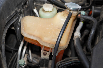 A close-up shows the expansion tank of a car's cooling system containing orange liquid, emphasizing engine maintenance.