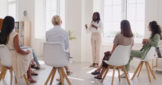 Women group listening to speaker and coach. They sit in a circle as leadership training unfolds, exchanging notes and discussing business goals. Clear teamwork and leadership concept.
