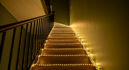 Festive staircase illuminated by warm yellow string lights. Holiday home interior decoration for Christmas and New Year's Eve