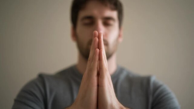 Close-up shot of a young man with closed eyes meditating and performing mudras with his hands, conveying peace and mindfulness in a serene setting.
