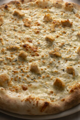 Crisp white pizza topped with chicken chunks and melted cheeses, golden bubbling crust, herb flecks and garlic aroma, decadent