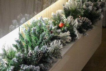 Snow-dusted Christmas garland with pine cones and red ornaments decorates a modern interior, creating a warm and festive holiday atmosphere.