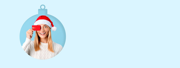 A cheerful woman wearing a Santa hat holds a gift card while smiling brightly against a light blue...