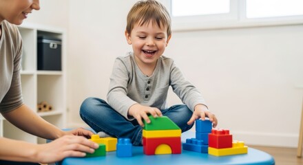 Preschooler in casual attire plays with blocks with therapist, laughing, in a therapy setting. Child development assessment.