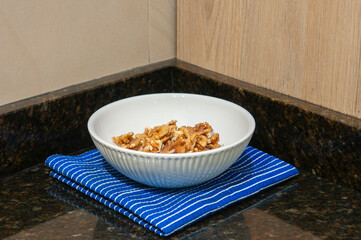 Close-up of shelled walnuts in a white bowl on a blue striped tablecloth and a marble countertop.
