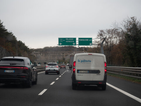 Italy A4 highway traffic with cars and Fiat Doblo van on a cloudy day, indicating direction to Milan and Venice