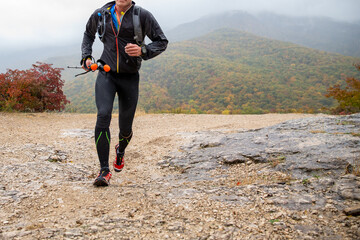 Man running mountain marathon in rain with trekking poles in his hands