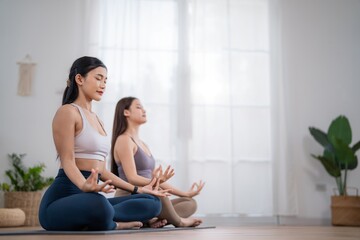 Two people practice yoga and meditation indoors in a bright room with plants and natural light
