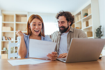 Happy Couple Reviews Documents Together At Home While Smiling, Working On Laptop And Planning