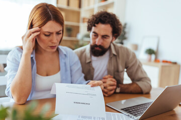 Confused Couple Reviews Important Documents at Home Office Beside Laptop, Looking Concerned