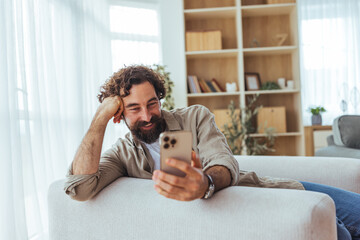 Smiling Bearded Man Relaxing on Couch While Using Smartphone at Home Living Room Scene